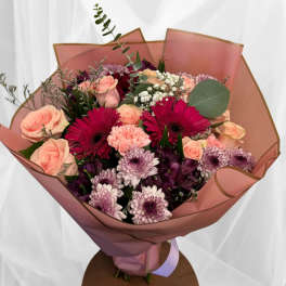 Hand-tied bouquet of pink roses, magenta gerbera daisies and lavender mums in pink wrapping
