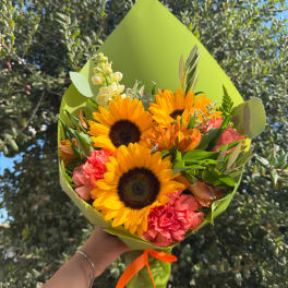 Handheld bouquet with sunflowers, pink carnations, and green wrapping