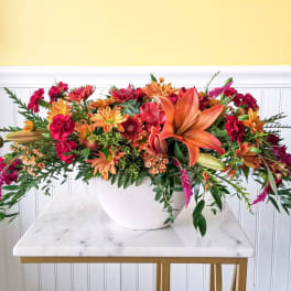 Long floral arrangement in a white bowl with orange lilies and red-orange blooms