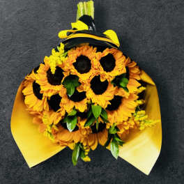 Bouquet of bright yellow sunflowers with green accents wrapped in yellow paper and black ribbon