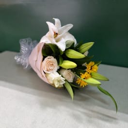 Bouquet of white lilies, pale roses, and yellow flowers wrapped in pink paper