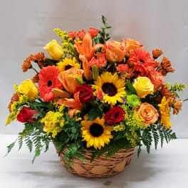 Mixed bouquet of roses, lilies, sunflowers, and gerbera daisies in a wicker basket