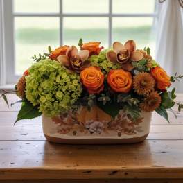 Low fall centerpiece with orange roses, orchids, and green hydrangeas in a rectangular ceramic container