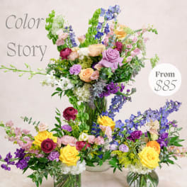 Colorful mixed flower arrangements with roses, delphinium, and orchids in glass vases