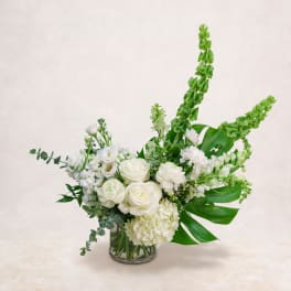 White floral arrangement in a clear glass vase with tall green spikes