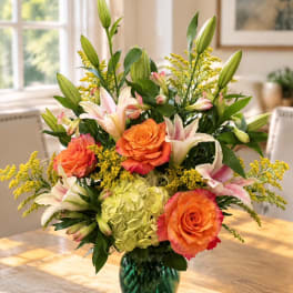 Orange roses and lilies arranged in a green glass vase