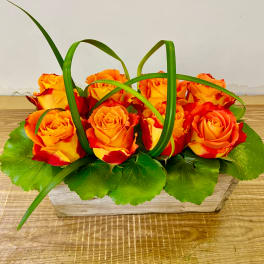 Orange and red roses arranged in a low rectangular glass vase