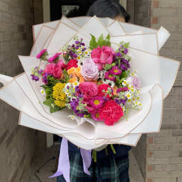 Large bouquet of pink, purple, and yellow flowers wrapped in white paper