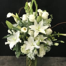 White lilies, calla lilies, and roses arranged in a tall glass vase