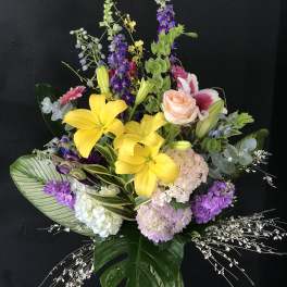 Tall mixed bouquet with yellow lilies, pink roses, and purple flowers in a glass vase