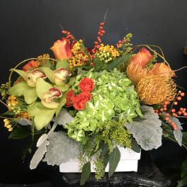 Mixed floral arrangement with orchids, roses, and hydrangea in a white container