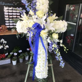 White floral standing cross with blue ribbon and yellow roses