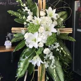 White lilies and roses arranged on a wooden cross with green foliage