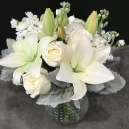 White lilies and roses in a glass vase with silver foliage