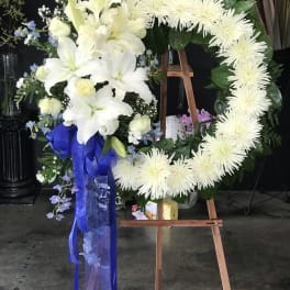 White floral funeral wreath on an easel with a blue ribbon