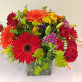 Mixed bouquet of red and orange flowers in a clear square vase