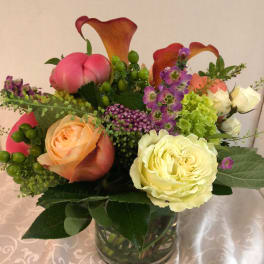 Mixed bouquet in a glass vase with roses, calla lilies, and purple accent flowers