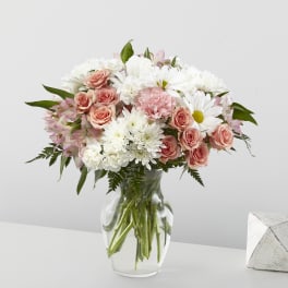 Mixed bouquet of white daisies and mums with peach roses in a clear glass vase