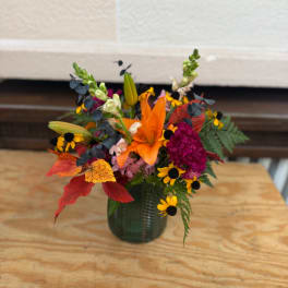 Orange lily bouquet in a dark green vase with autumn flowers