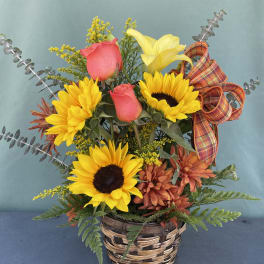 Basket arrangement with sunflowers, pink roses, and a yellow lily with plaid ribbon