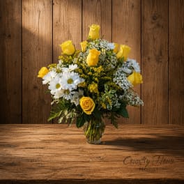 Yellow roses and white daisies arranged in a clear glass vase