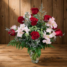 Red roses and pale pink flowers arranged in a clear glass vase