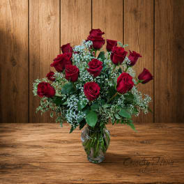 Red roses arranged in a clear glass vase with white filler flowers