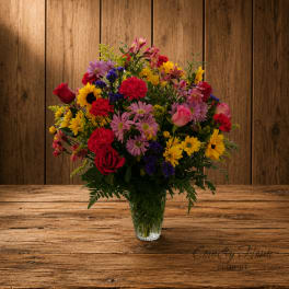 Mixed bouquet of red, pink, yellow, and purple flowers in a clear glass vase