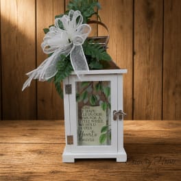 White memorial lantern with ribbon and greenery on a wooden surface