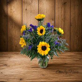 Sunflower bouquet in a clear glass vase with purple filler flowers