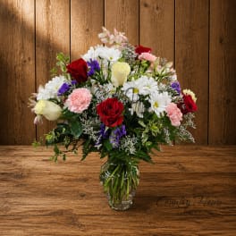 Mixed bouquet of roses, daisies, and carnations in a clear glass vase