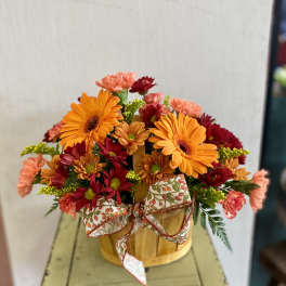 Orange and red mixed flowers arranged in a wooden basket with a patterned bow
