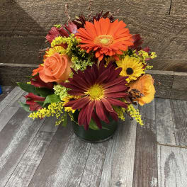 Mixed bouquet of orange, yellow, and burgundy flowers in a dark vase