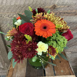 Mixed bouquet of red, orange, and yellow flowers in a green glass vase