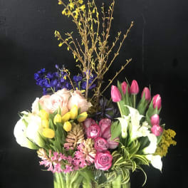 Mixed bouquet in a clear glass vase with tulips, roses, calla lilies, and orchids