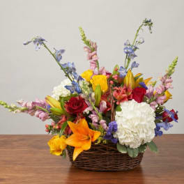 Mixed flower arrangement in a wicker basket with lilies, roses, hydrangea, and tall blue blooms
