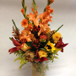 Tall mixed bouquet with orange gladiolus, red lilies, and yellow blooms in a burlap-wrapped vase