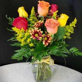 Mixed roses and chrysanthemums in a glass vase with yellow filler flowers