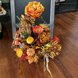Autumn floral arrangement with orange blooms, pumpkins, and fall leaves in a basket.