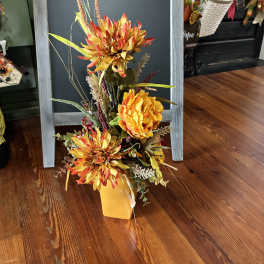 Tall autumn floral arrangement in a yellow vase with orange blooms