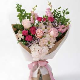 Bouquet of pink roses and pale hydrangeas with greenery, wrapped in paper and tied with a pink ribbon.