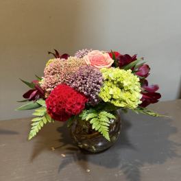 Mixed bouquet in a round glass vase with pink, red, and green blooms