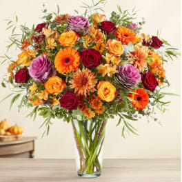 Mixed bouquet of roses, gerbera daisies, and orange blooms in a clear vase