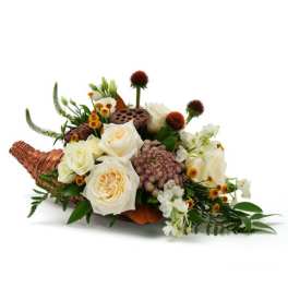 Cornucopia centerpiece with cream roses, white blossoms, and small yellow flowers in a woven horn basket.
