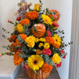 Pumpkin-themed bouquet with yellow roses, gerbera daisies, and orange marigolds in a pumpkin vase