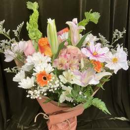 Mixed bouquet of lilies, roses, daisies, and orange gerbera daisies wrapped in pink paper
