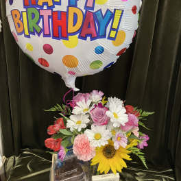 Birthday balloon above a mixed flower arrangement in a wooden box with chocolates