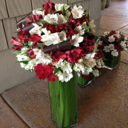 Red and white flower arrangement in a tall green vase with dark ribbon accents