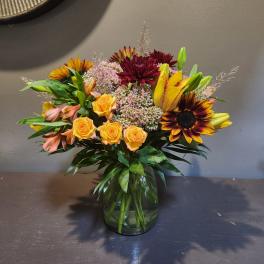 Mixed bouquet of sunflowers, roses, lilies, and chrysanthemums in a glass vase