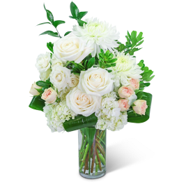White roses and chrysanthemums in a clear glass vase with green foliage